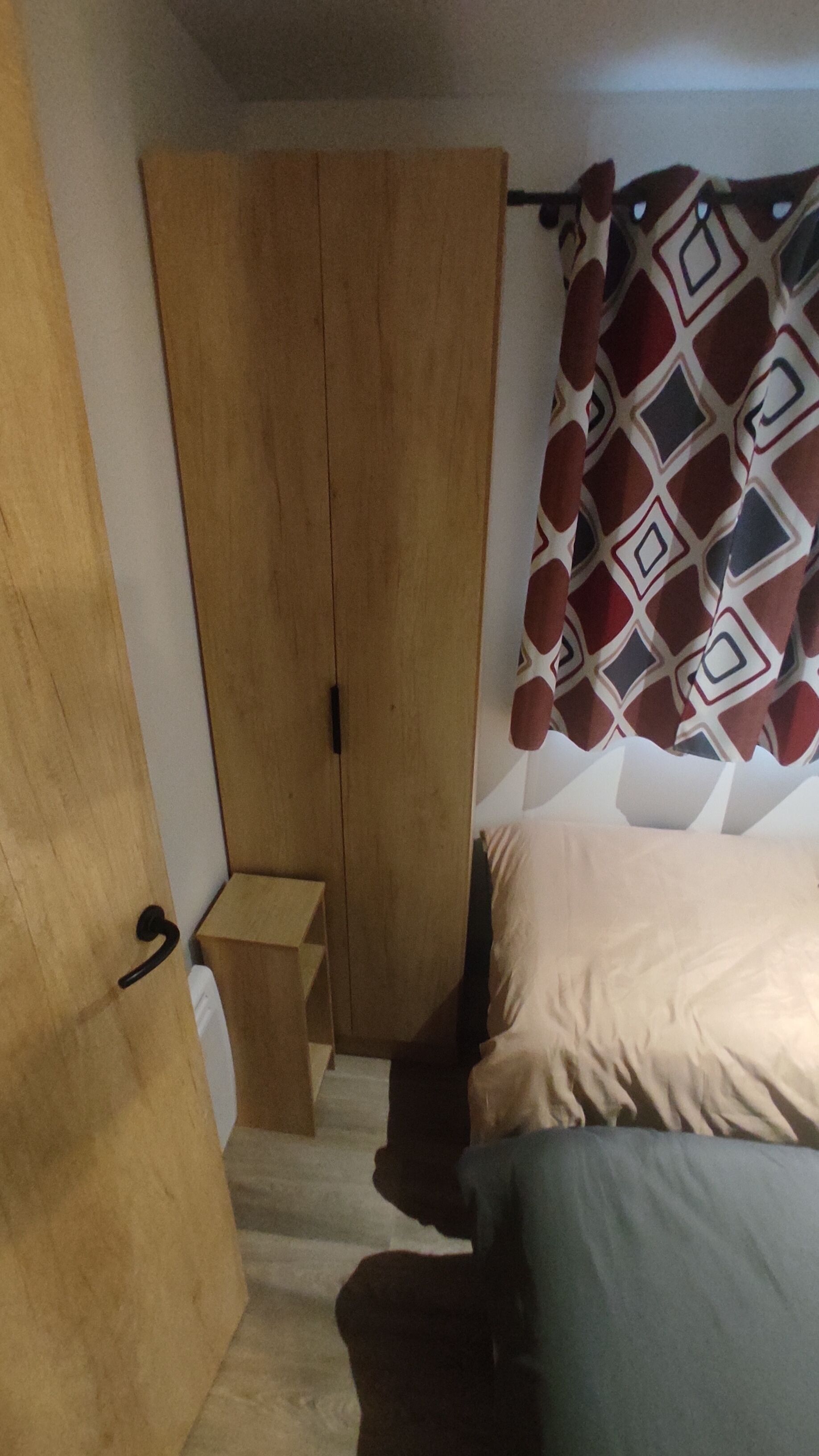 Una camera da letto con un armadio in legno, un letto con copripiumino fantasia e un piccolo sgabello in legno.