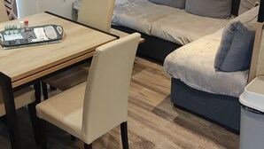 Una sala de estar con un sofá, una mesa de comedor con sillas y una ventana con cortinas estampadas.