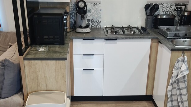 Una cocina moderna con armarios blancos, estufa a gas, cafetera y un cubo de basura.