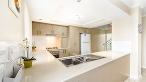 A modern kitchen with a central island, stainless steel appliances, and light-colored cabinetry. - Serenity Townhouse - Mandurah (Mandurah)