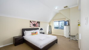 A bedroom with a large bed, a nightstand, a desk with a computer, a chair, and a window. - Serenity Townhouse - Mandurah (Mandurah)