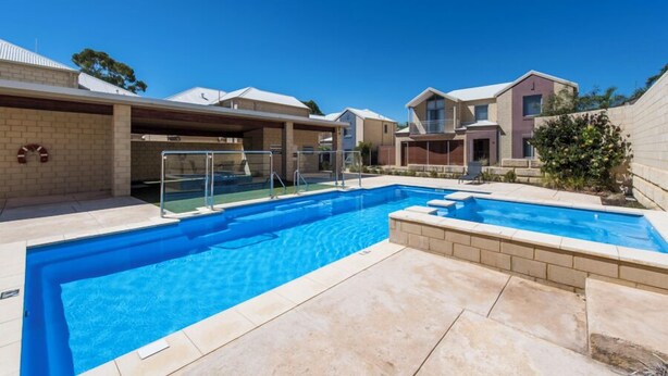 A swimming pool with a clear blue water, surrounded by a patio area with beige tiles. - Serenity Townhouse - Mandurah (Mandurah)