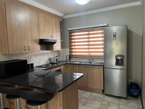 A kitchen with wooden cabinets, a stainless steel refrigerator, a sink, and a stove. - Spacious Apartment Near Gautrain, Gallagher & MOA (Johannesburg)