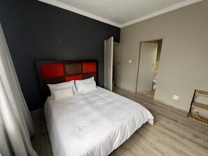 A bedroom with a bed, a headboard, and a door leading to a bathroom. - Spacious Apartment Near Gautrain, Gallagher & MOA (Johannesburg)