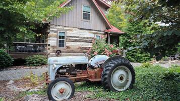 A rustic wooden house with a red roof, a vintage tractor parked in front, and a gravel driveway.