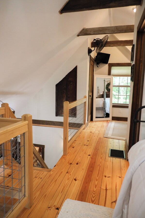 A wooden staircase with a metal railing, a wooden floor, a white wall, a ceiling fan, and a window with a view of greenery.