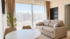 Ein Wohnzimmer mit einem beigefarbenen Sofa, einem runden Tisch und transparenten Vorhängen.