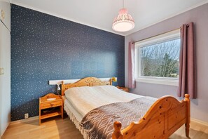 Een slaapkamer met een muur met stermotief, een houten bed, een nachtkastje en een raam met gordijnen, plus een hanglamp.