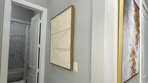 Un corridoio con pavimento a scacchi, una porta che conduce al bagno e due quadri appesi al muro.