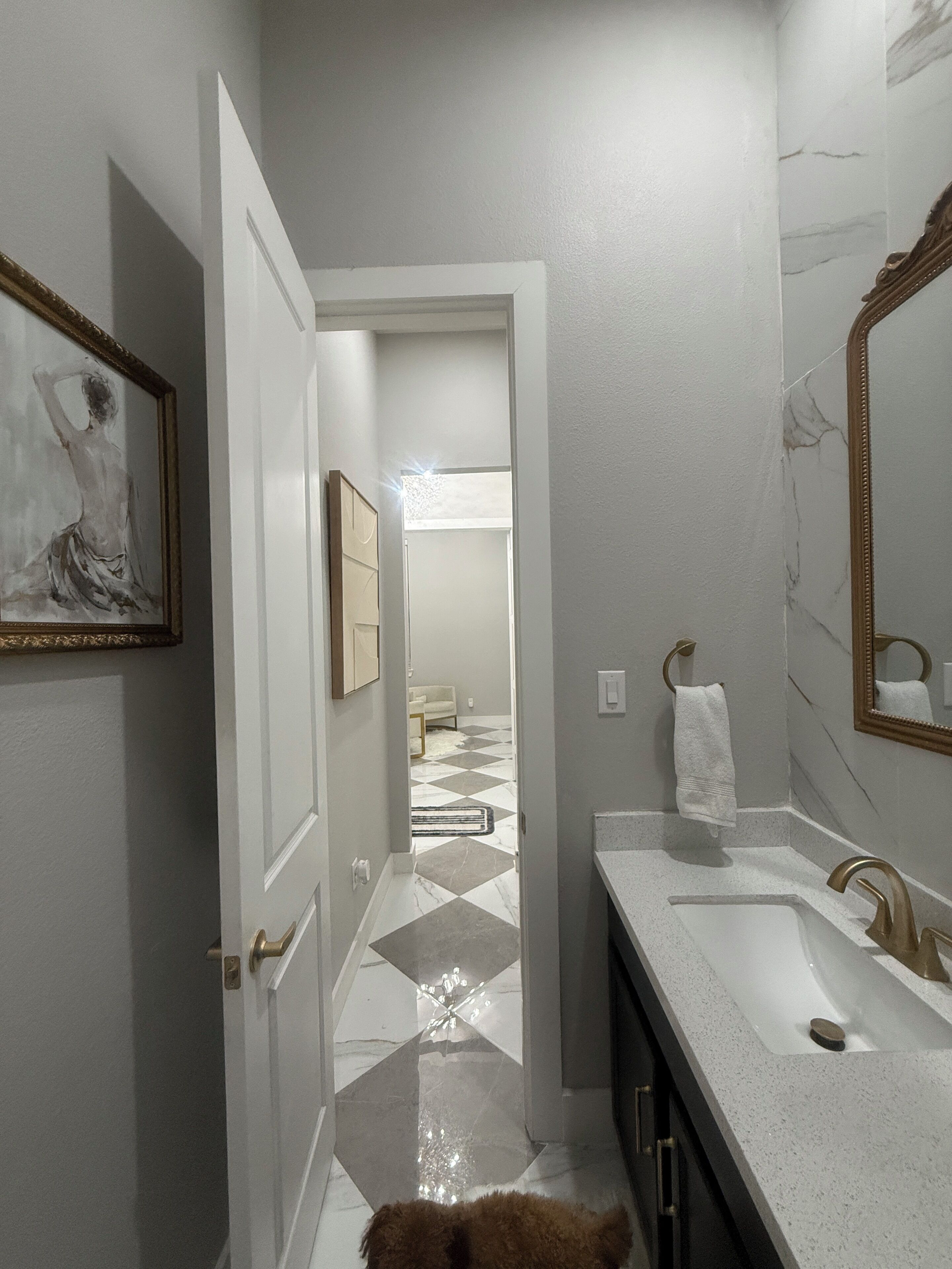 Uma casa de banho com uma pia branca, um espelho e uma porta que dá para outro espaço.