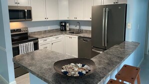 Una cocina con armarios blancos, un refrigerador de acero inoxidable, un microondas y una cafetera.