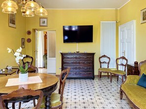 A room with a dining table, chairs, a sofa, a fireplace, a television, and a patterned floor. - Una Finestra sul Lago by Interhome (Bellano)