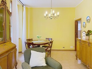 A dining area with a chandelier, a round table, chairs, a sofa with a pillow, a wooden cabinet, and a mirror. - Una Finestra sul Lago by Interhome (Bellano)