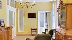 A living room with a chandelier, a television, a wooden cabinet, and a green armchair. - Una Finestra sul Lago by Interhome (Bellano)