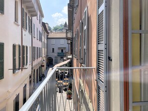 A narrow street with buildings on either side, a metal railing, and outdoor seating. - Una Finestra sul Lago by Interhome (Bellano)