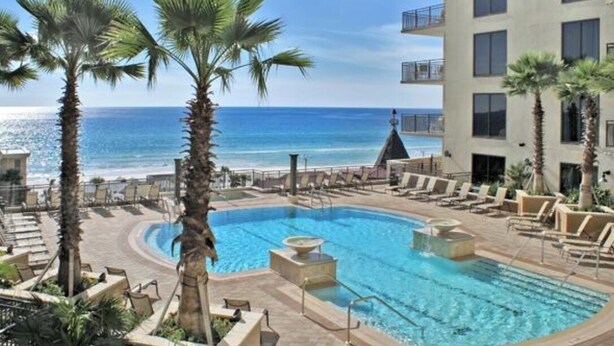 A pool area with palm trees, a clear blue sky, and a view of the ocean. - Labor Day Opening🌴Last minute PCB Getaway  The Pink Panama at Origin at Seahaven (Panama City Beach)