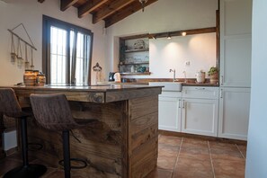 Eine Küche mit einer Holztheke, Barhocker, weißen Schränken und einem Fenster.