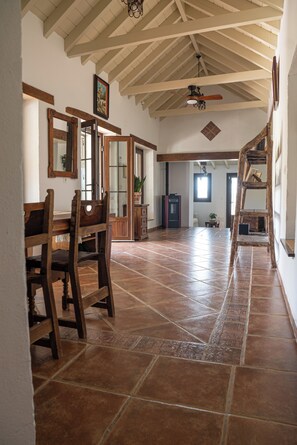 Ein geräumiger Raum mit hoher Decke, Holzbalken, Fliesenboden und Deckenventilator.