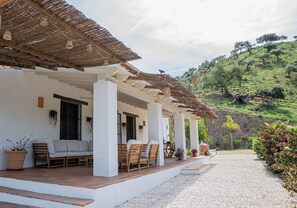 Ein überdachter Außenbereich mit Terrasse, ein weißes Gebäude mit Säulen und Blick auf eine Hügelkuppe.