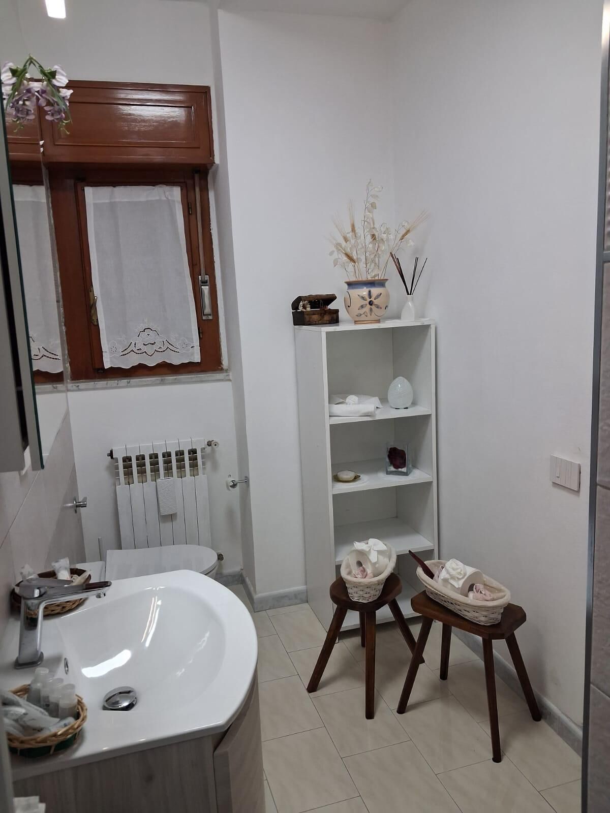 A bathroom with a white sink, a mirror, a wooden cabinet, and a shelf with toiletries.