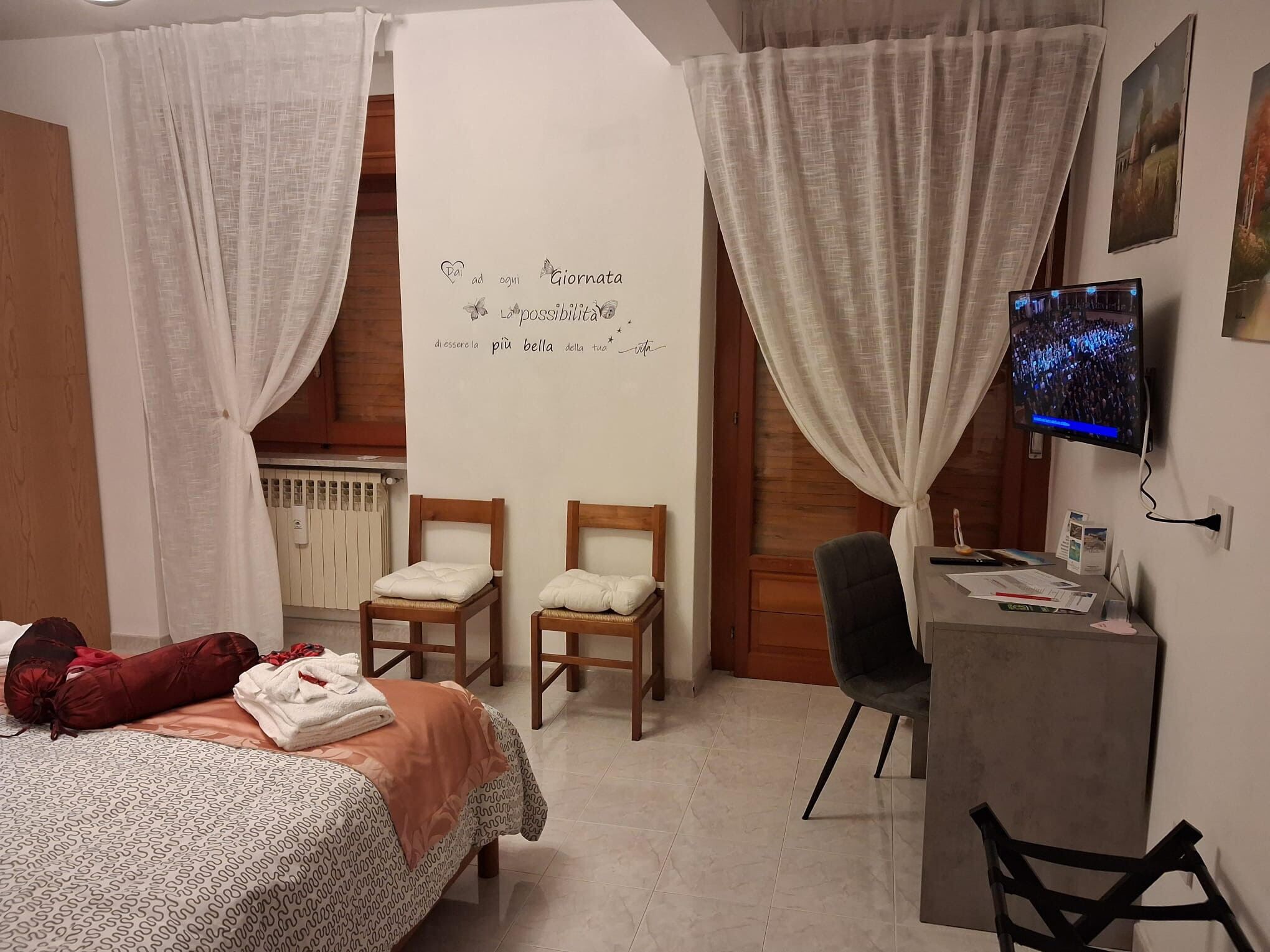 Une chambre à coucher comprenant un lit, deux chaises, un bureau, un téléviseur et un mur orné d’une citation inspirante.