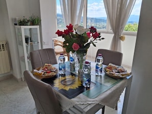 A dining area with a table set for two, a vase with flowers, water bottles, and a basket of bread.