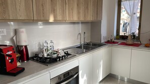 Una cocina moderna con estufa a gas, cafetera, lavaplatos y ventana con vista a edificios.
