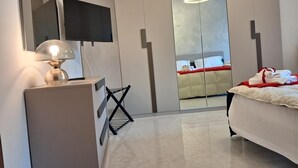Una habitación de hotel moderna con cama, televisor, escritorio con lámpara, espejo y armario.