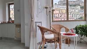 Habitación con vistas a un paisaje urbano, sillas de mimbre, una mesita con mantel rojo y una planta en maceta.