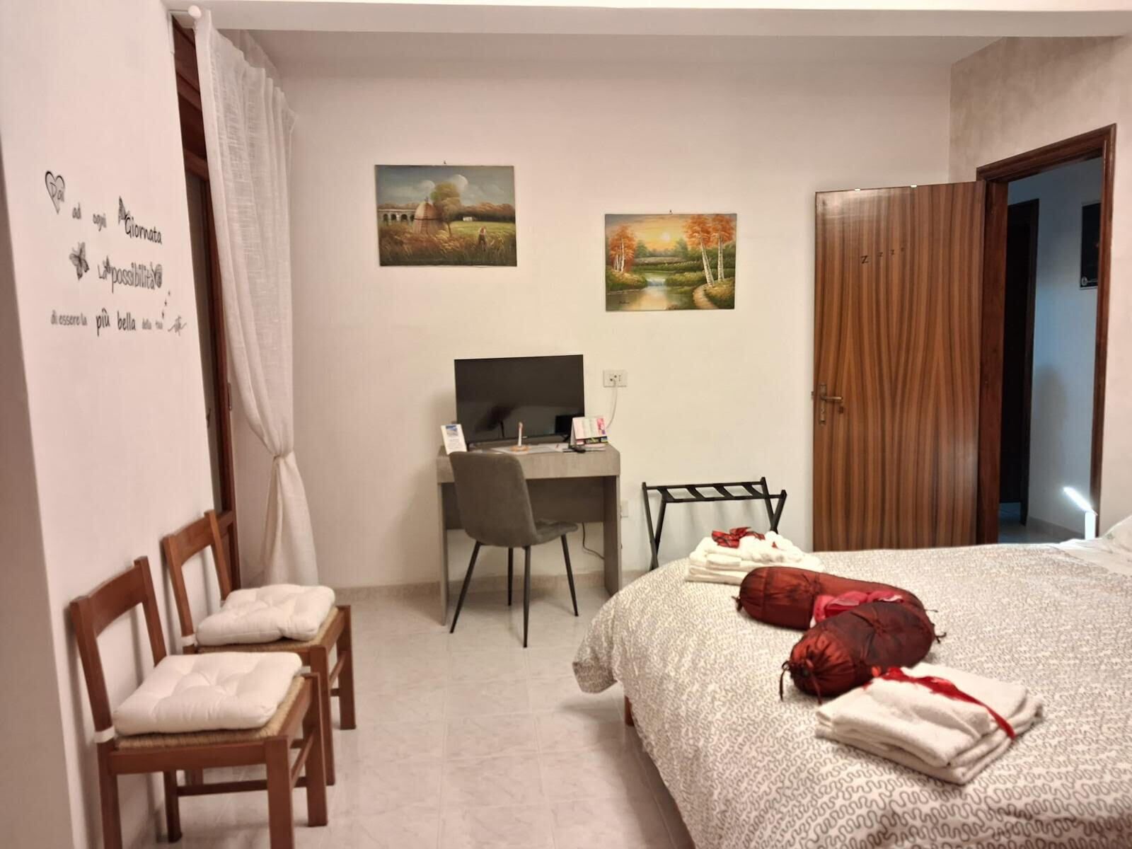 A bedroom with a bed, a desk, a chair, and two paintings on the wall.