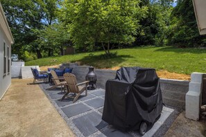 En udendørs patio med grill, stole og en gulv belagt med natursten.