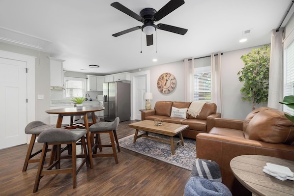 Un salon moderne comprenant un coin repas, un ventilateur de plafond, une horloge murale et une vue sur la cuisine.