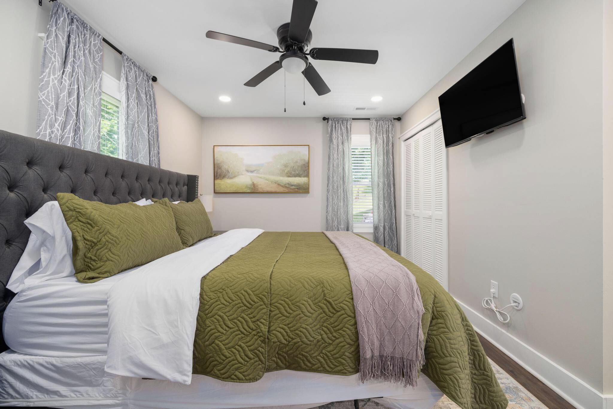 Un dormitorio con cama, ventilador de techo, televisión y una obra de arte en la pared.