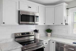 A modern kitchen with white cabinetry, stainless steel appliances, and a marble countertop.