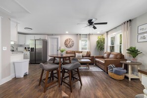 A modern living room with a dining area, a kitchen, and a ceiling fan.