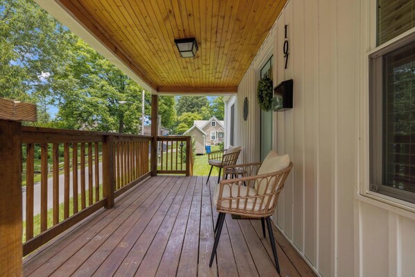 A wooden deck with a railing, two wicker chairs, a hanging light fixture, and a house number 107.