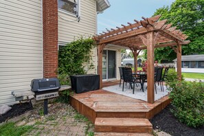 A wooden deck with a pergola, a grill, and a table with chairs.
