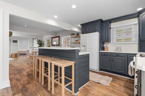 A modern kitchen with dark cabinets, a central island with stools, and a dining area with wooden tables.
