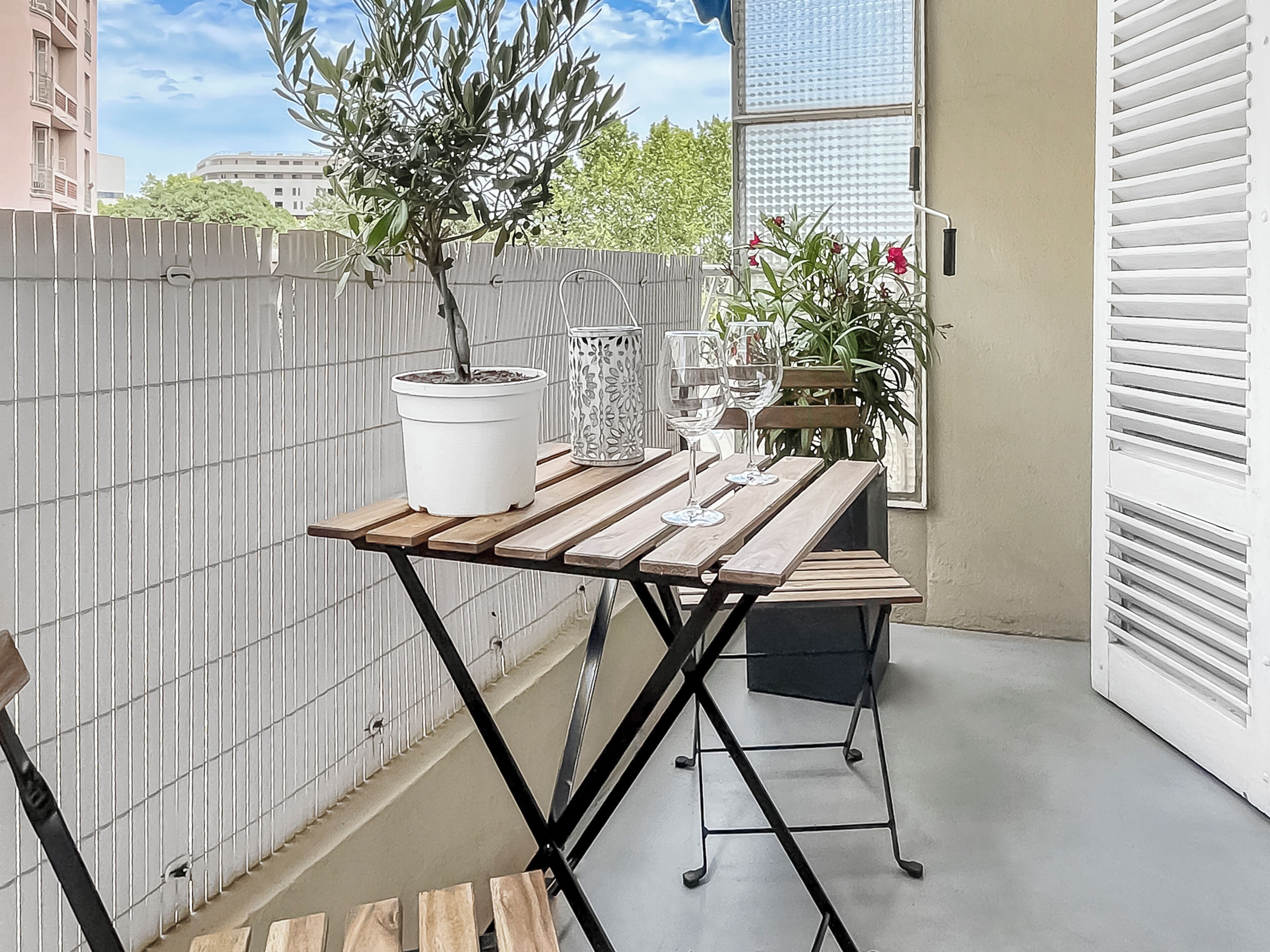 Ein Balkon mit Holztisch, Topfpflanzen und einem Metallstuhl.