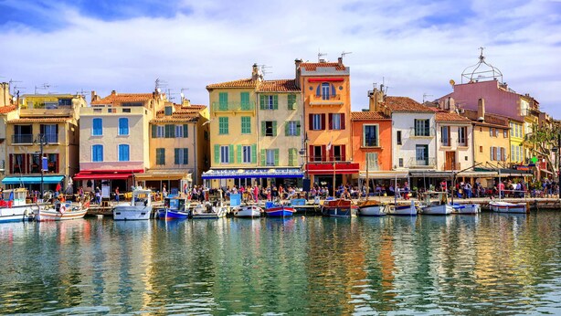 Uma orla marítima com edifícios coloridos, barcos atracados na costa e pessoas reunidas no calçadão.