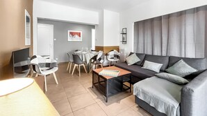 Uma sala de estar moderna com um sofá, uma mesa de jantar posta para quatro e uma televisão.