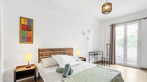 Um quarto com uma cama, duas mesas de cabeceira, uma luminária, uma cadeira, uma mesinha e vista para o exterior através de uma porta deslizante.