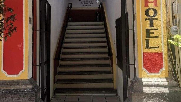 Entrada de hotel con una escalera que lleva a una puerta, un letrero encima de la puerta y un cartel en la pared a la derecha.