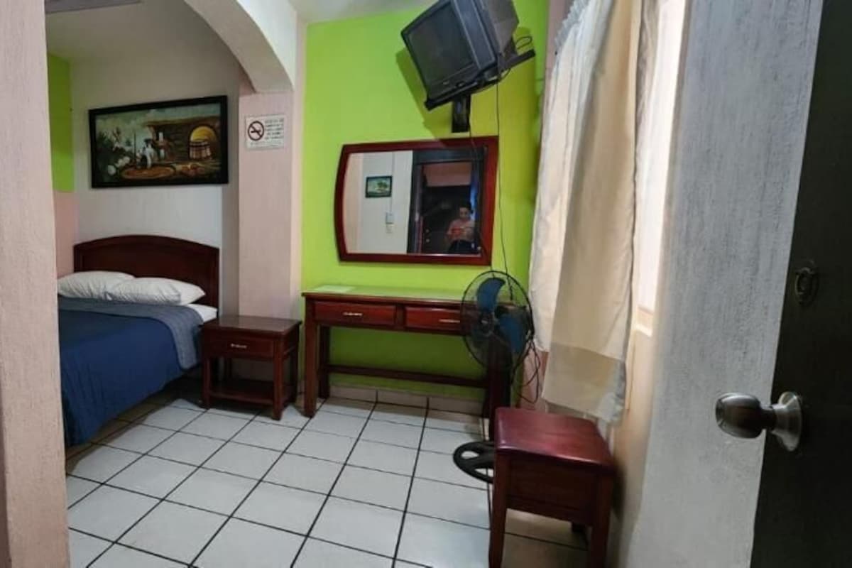 Una habitación con una cama, un escritorio, una silla, un televisor y una puerta.