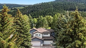 Il s’agit d’une propriété résidentielle comprenant une maison à deux étages, un garage et une allée, le tout entouré d’une forêt de conifères dense et avec une colline en arrière-plan.