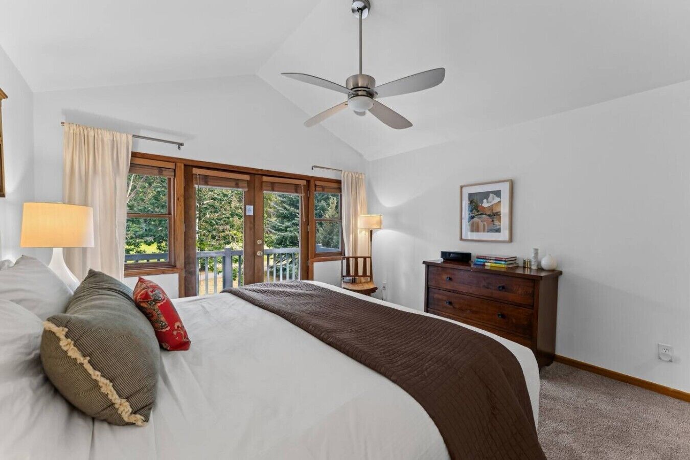 A bedroom with a bed, a dresser, a ceiling fan, and a view of the outdoors.