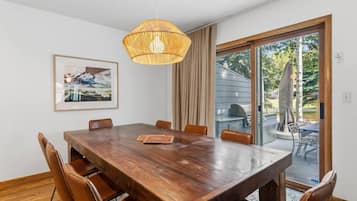 Et spiseområde med et træbord, stole, en hængende lampe og udsigt til det frie gennem en glasdør.