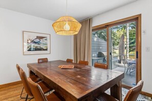 A dining area with a wooden table, chairs, a hanging light fixture, and a view of the outdoors through a glass door. - EagleVail Oasis on the 6th Fairway w/Hot Tub (Avon)
