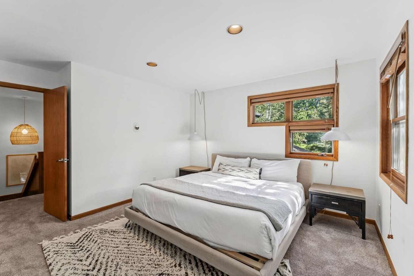 Une chambre à coucher avec un lit, des tables de chevet, une lampe suspendue, une fenêtre et une porte.