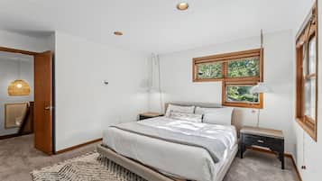 Une chambre à coucher avec un lit, des tables de chevet, une lampe suspendue, une fenêtre et une porte.